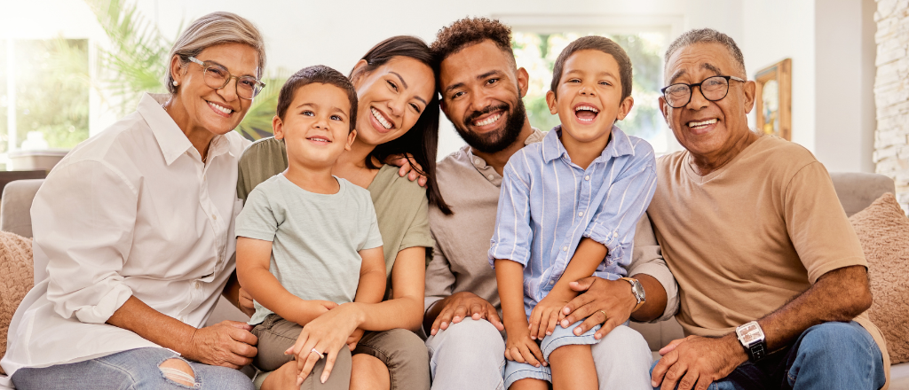 Three generations of a diverse family sitting together laughing on a couch